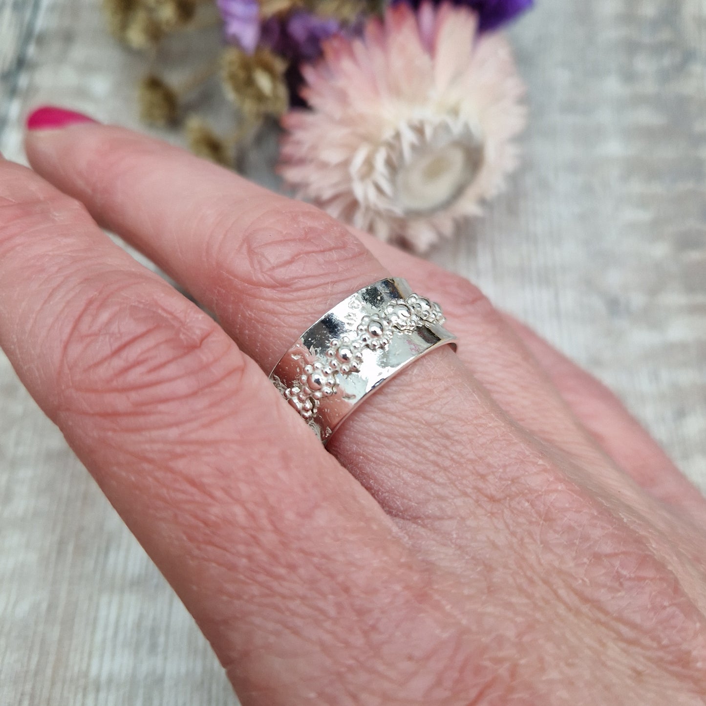  Approx. 10mm wide textured silver band with additional silver ring around the middle that spins independently detailed with repeating daisy flowers.