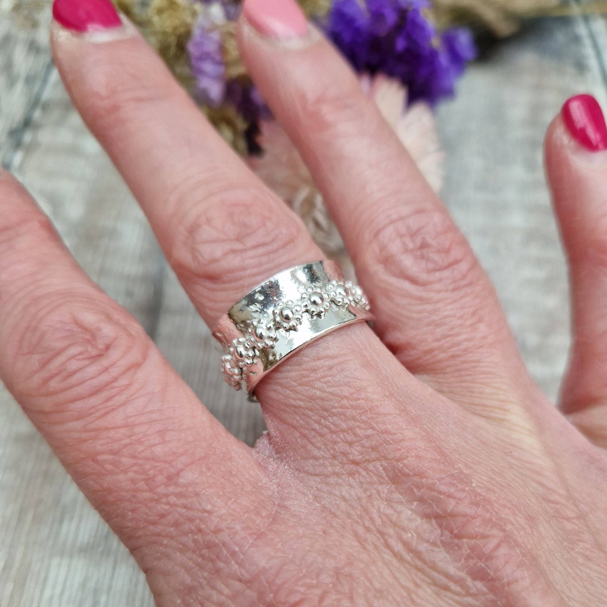  Approx. 10mm wide textured silver band with additional silver ring around the middle that spins independently detailed with repeating daisy flowers.