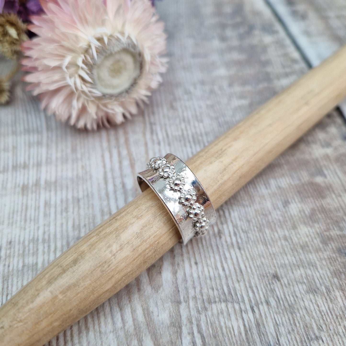  Approx. 10mm wide textured silver band with additional silver ring around the middle that spins independently detailed with repeating daisy flowers.