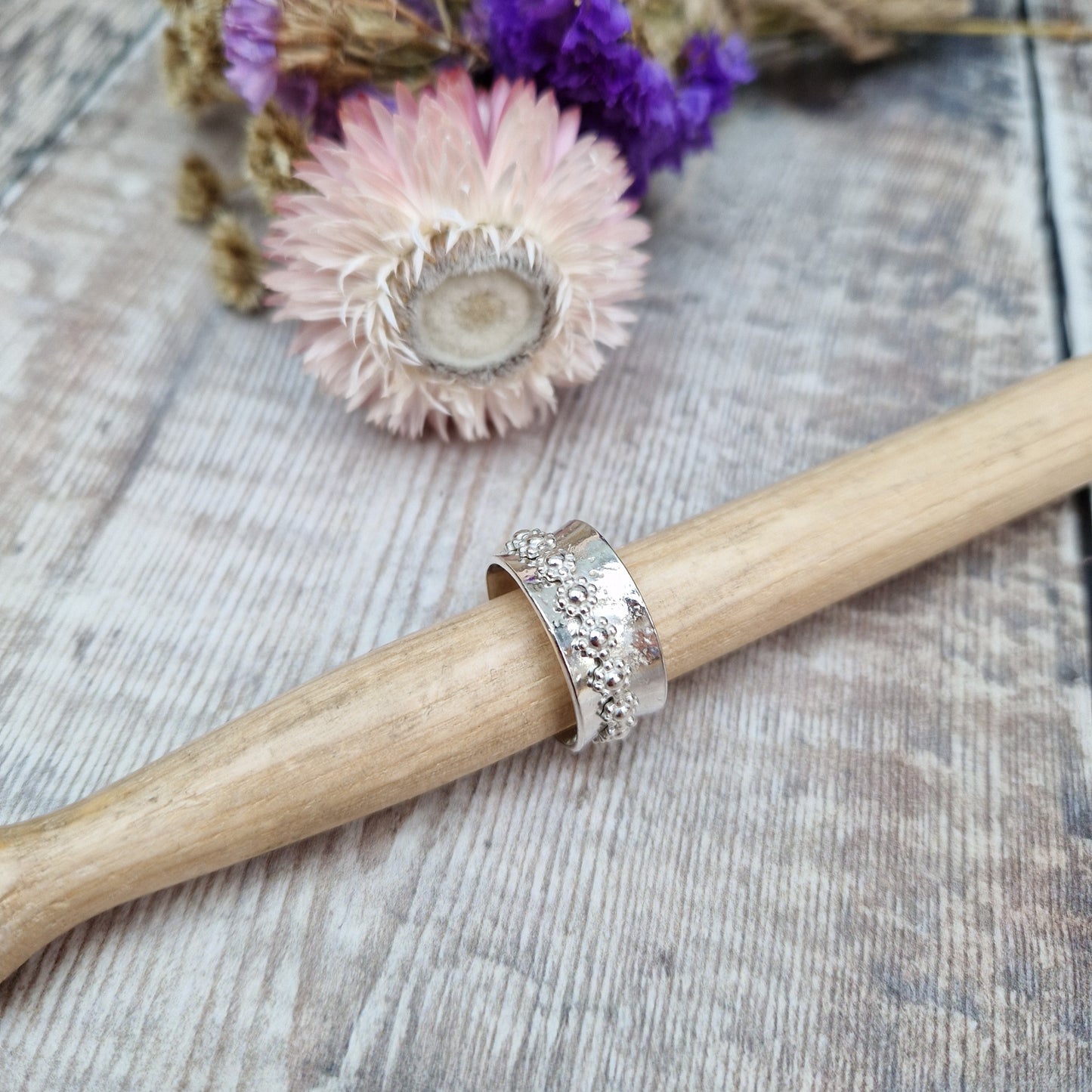  Approx. 10mm wide textured silver band with additional silver ring around the middle that spins independently detailed with repeating daisy flowers.