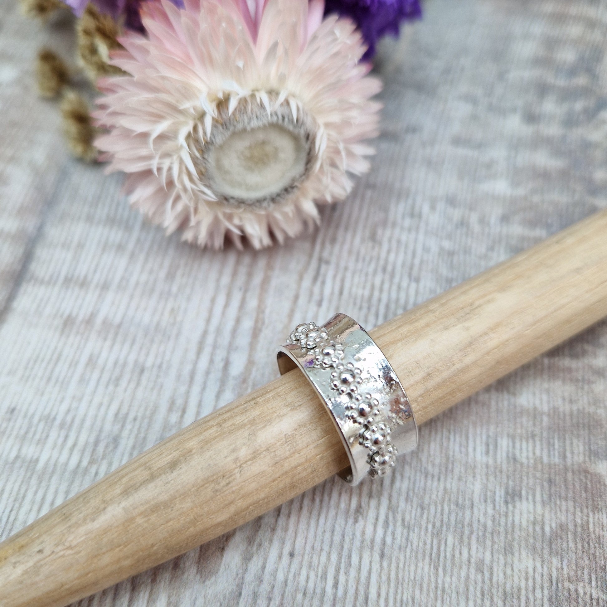  Approx. 10mm wide textured silver band with additional silver ring around the middle that spins independently detailed with repeating daisy flowers.