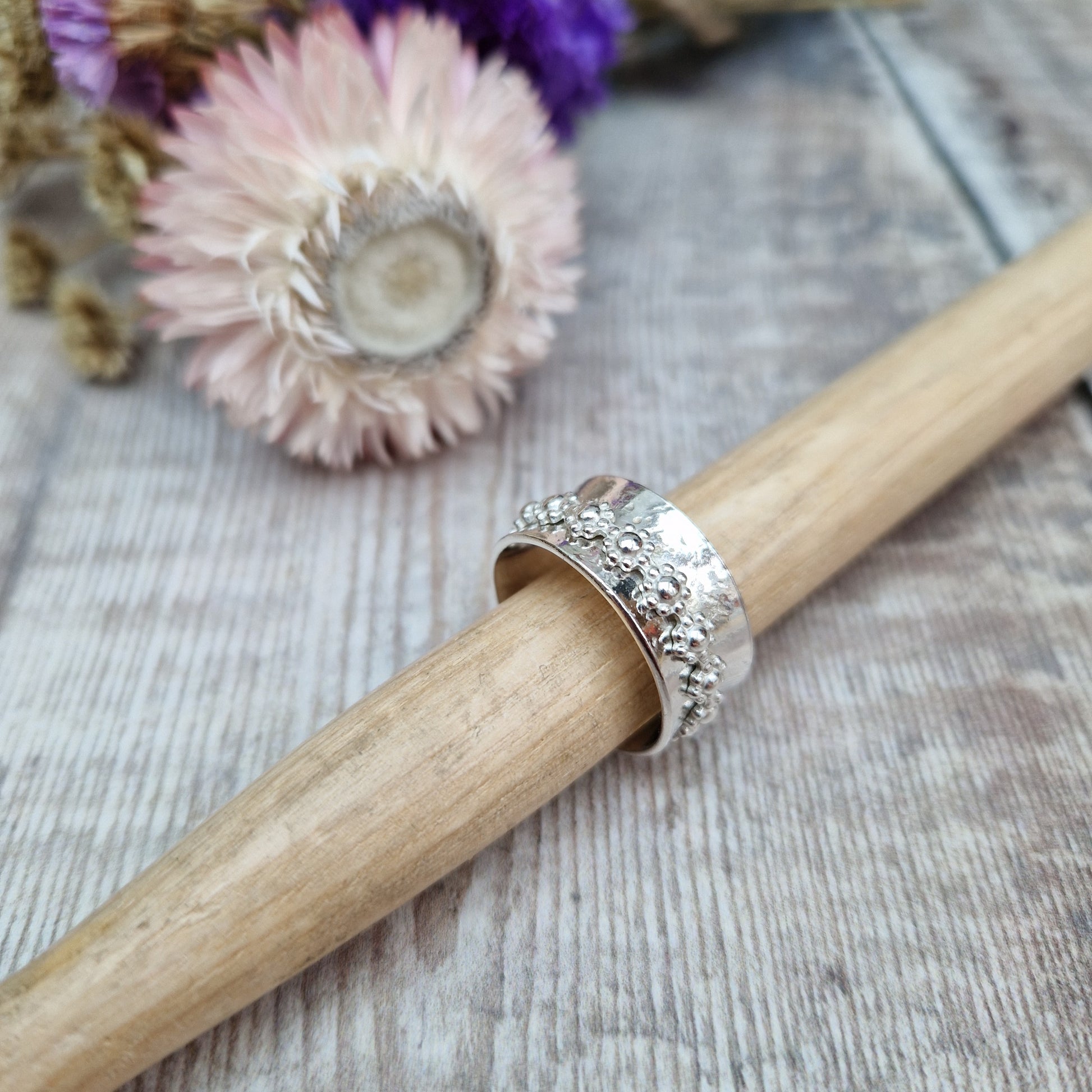  Approx. 10mm wide textured silver band with additional silver ring around the middle that spins independently detailed with repeating daisy flowers.