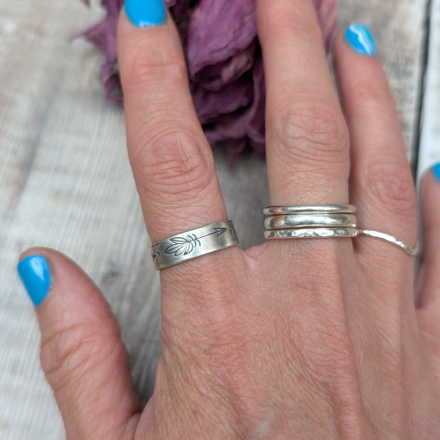 A hand showcasing a handmade silver ring with a 5mm wide band and hand-stamped feather designs. The ring has an oxidized finish.