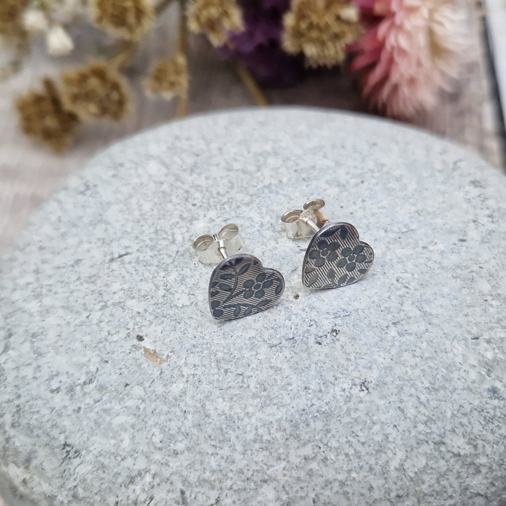 Each earring is an oxidised Sterling Silver heart shape on silver stud bar, stamped with a floral pattern of flowers with 5 petals and leaves. 