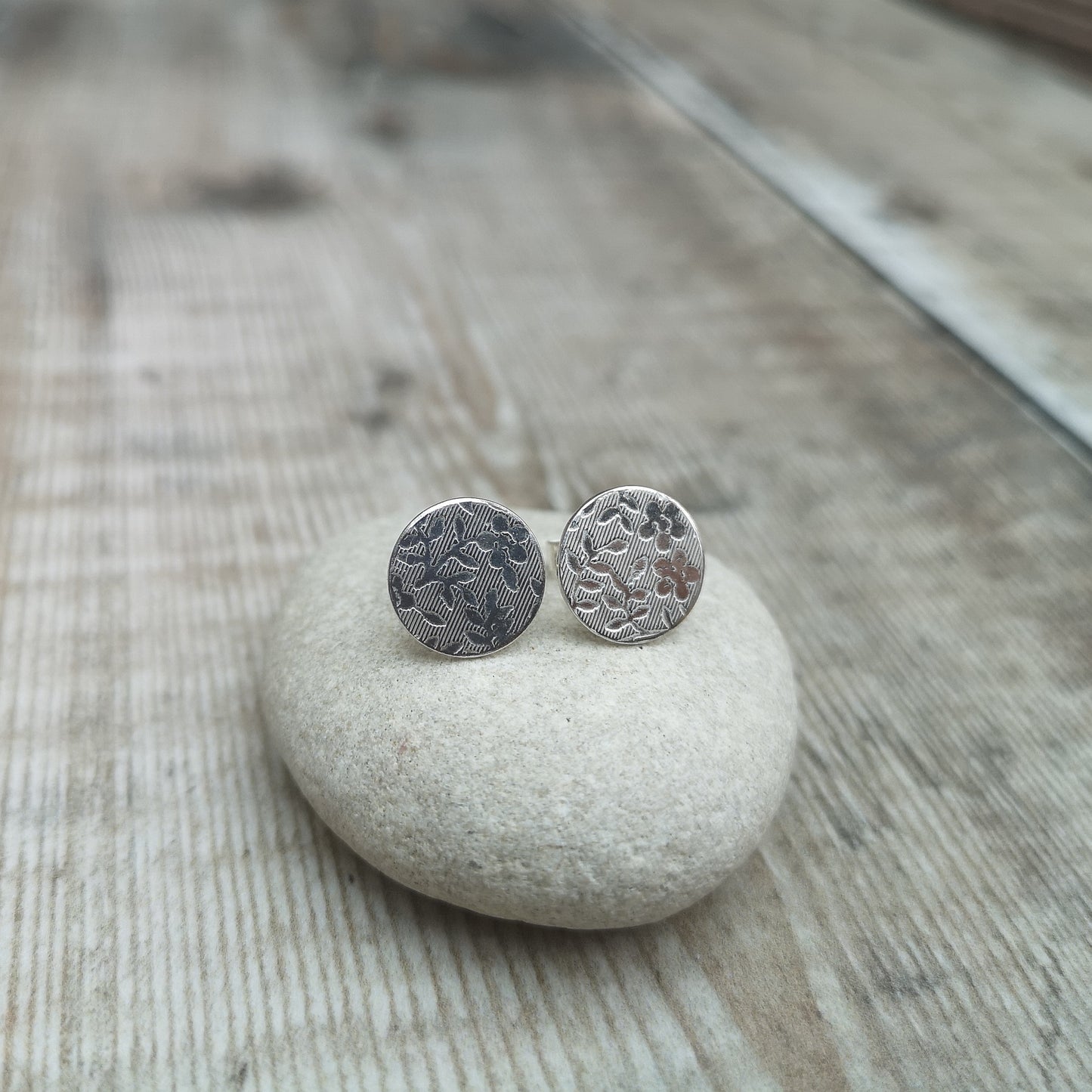 Each earring is a Sterling Silver disc on a silver stud bar, stamped with a floral pattern of flowers with 5 petals and leaves.