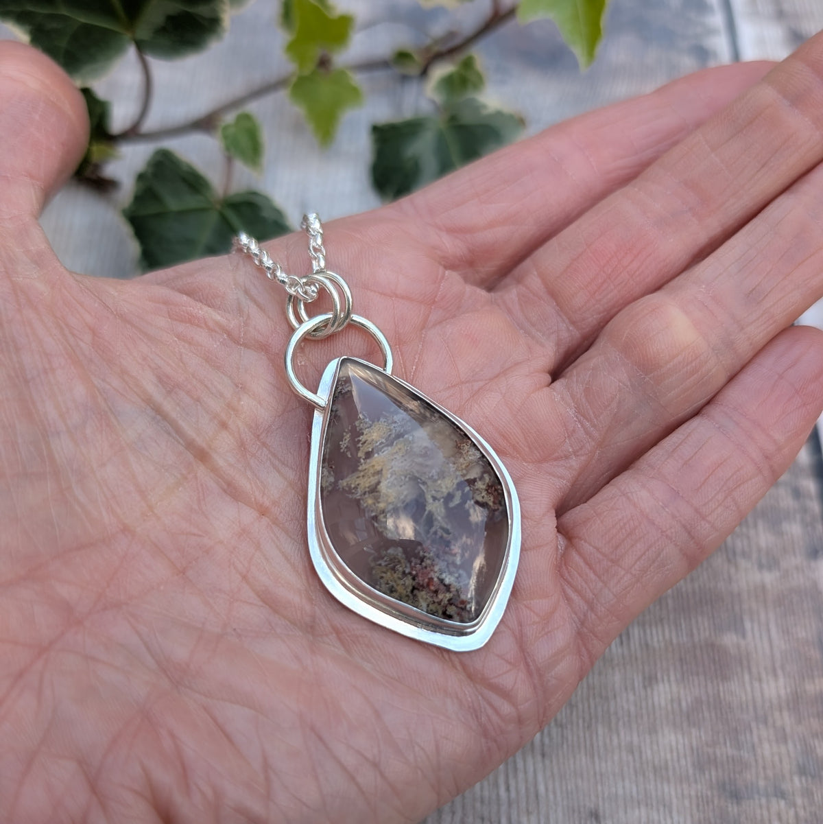 Garden Moss Agate Statement Gemstone Necklace resting in an open hand, showing the handmade recycled sterling silver setting and large polished gemstone with natural earthy coloured patterns.