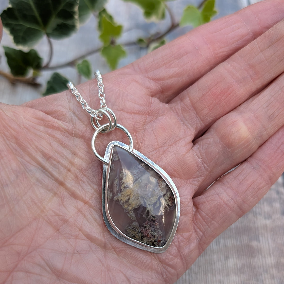 Garden Moss Agate Statement Gemstone Necklace handmade from recycled sterling silver, featuring a large irregular shaped gemstone with natural grey, cream and earthy coloured inclusions, resting in an open hand.