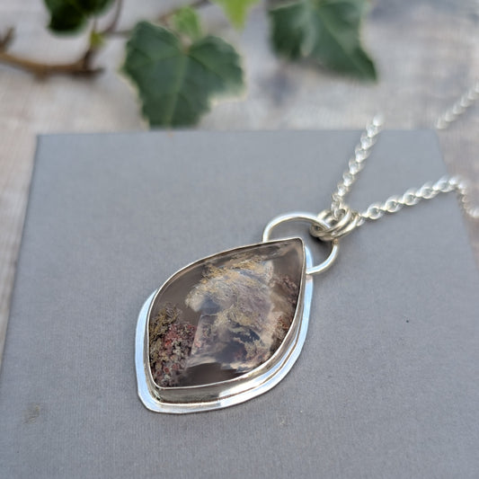 Close up of Garden Moss Agate Statement Gemstone Necklace resting on a grey background, showing the polished silver bezel setting and detailed natural inclusions within the stone.