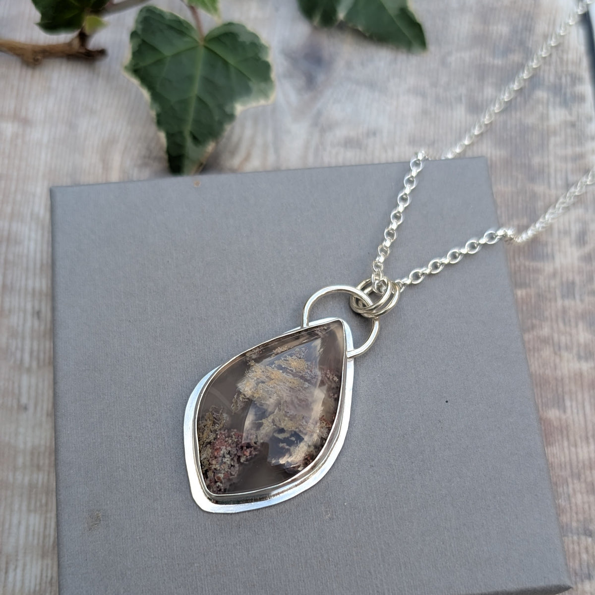Garden Moss Agate Statement Gemstone Necklace displayed on a grey background with its sterling silver chain, showing the irregular gemstone shape and handmade silver setting.