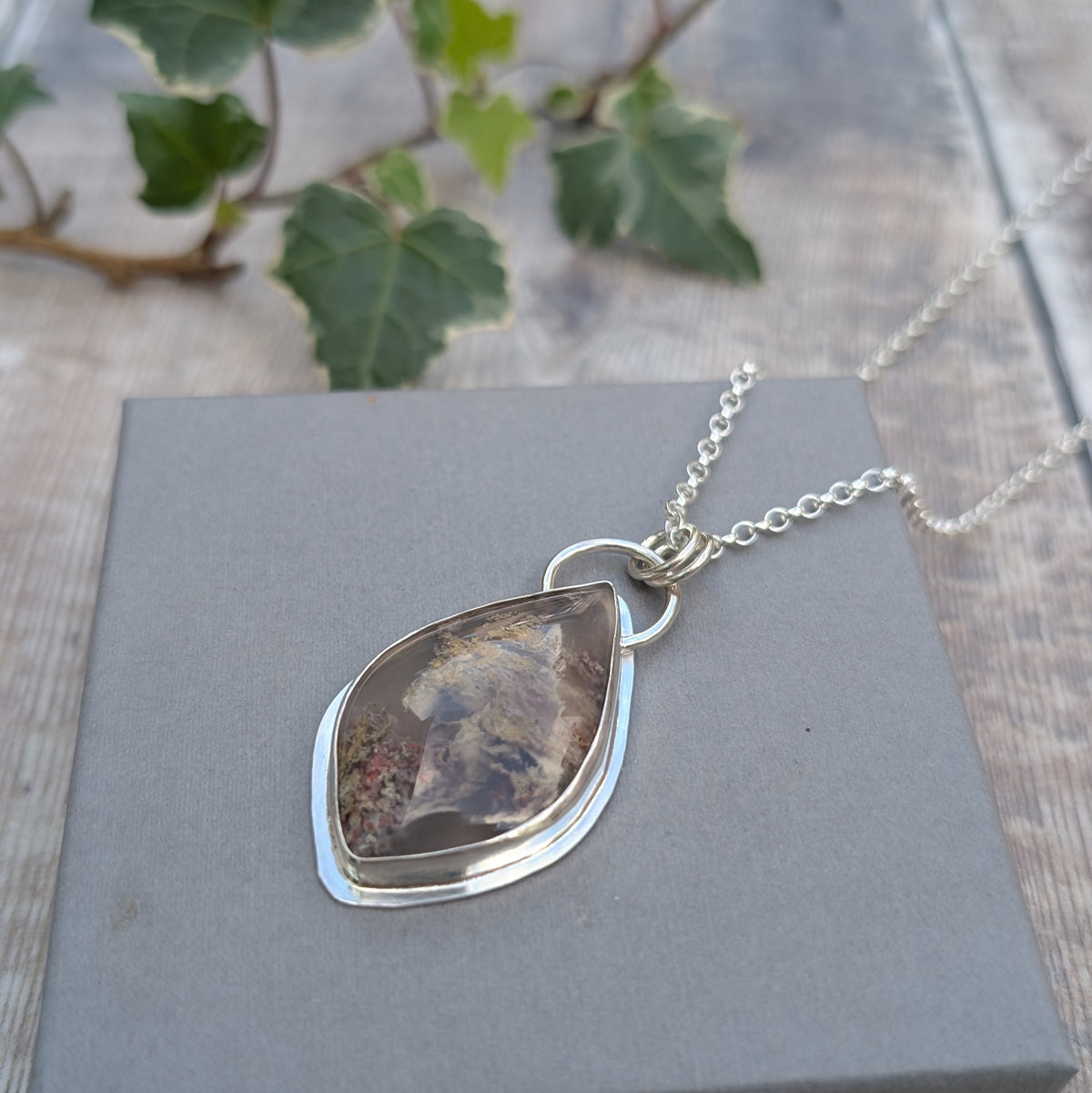 Garden Moss Agate Statement Gemstone Necklace lying on a grey background with a silver chain, showing the natural cream, grey and brown moss-like patterns in the gemstone.
