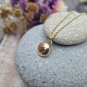 9ct Gold hammered pebble necklace. Pebble shaped pendant with hammered texture suspended from 9ct gold chain via two small, gold circular links.