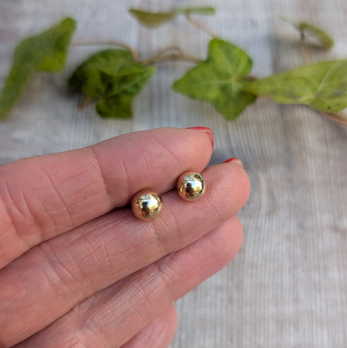 Small solid gold pebble stud earrings handmade from recycled 9ct gold, resting on fingertips to show their size.