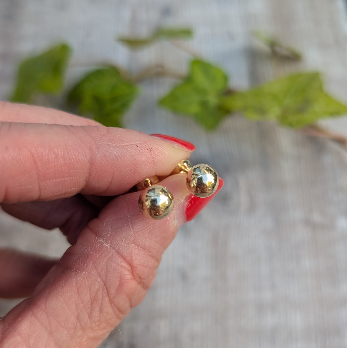 Close up of solid gold pebble stud earrings handmade from recycled 9ct gold, held between fingers to show their small rounded shape.