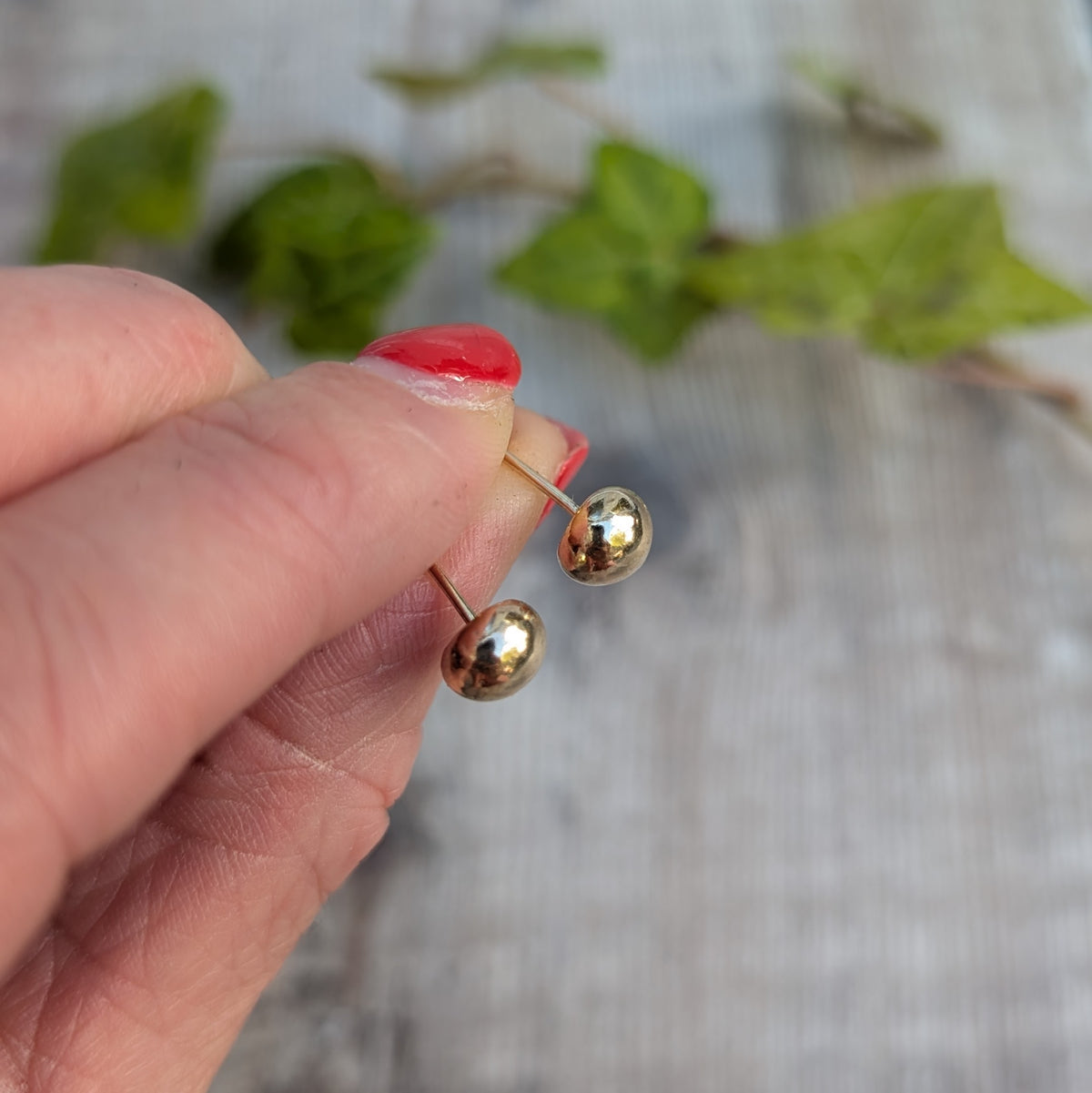 Side view of solid gold pebble stud earrings held by hand, showing the rounded gold pebbles and stud posts.