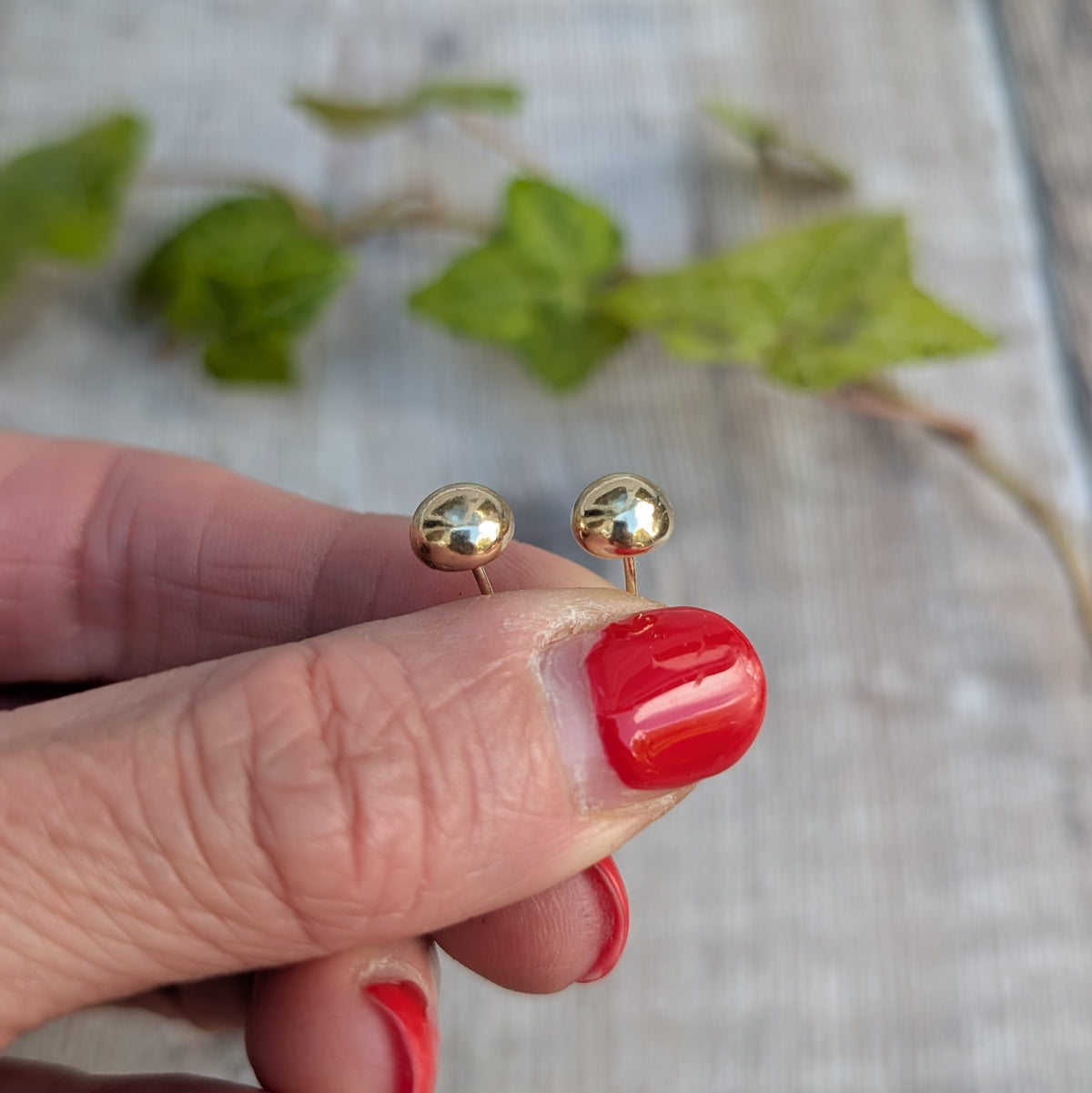 Front view of handmade solid gold pebble stud earrings held between fingers, showing their polished rounded finish.