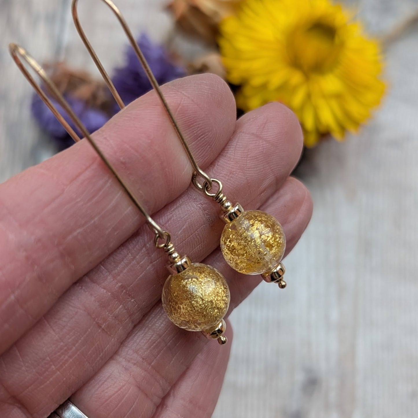 Close-up of gold filled earrings with round Venetian glass beads containing gold flecks, shown held in a hand to show size and detail.