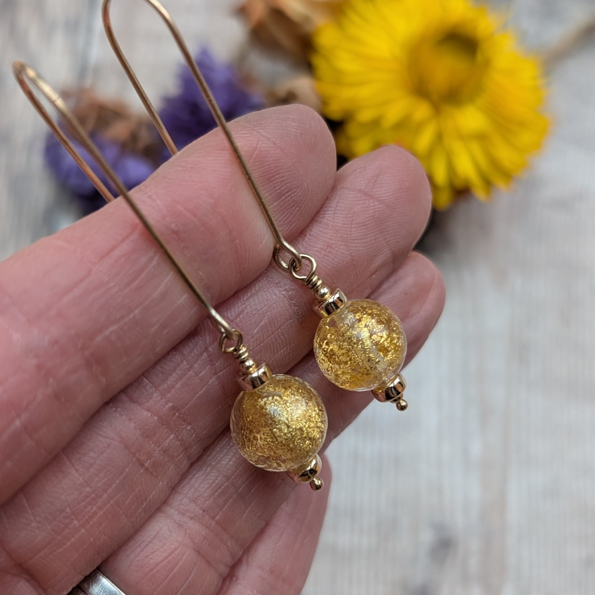 Close-up of gold filled earrings with round Venetian glass beads containing gold flecks, shown held in a hand to show size and detail.