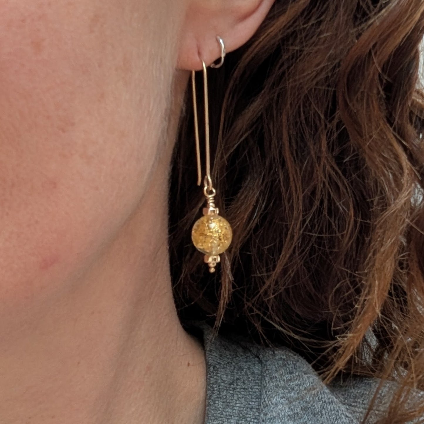 Gold filled long drop earring with a round Venetian glass bead containing gold flecks, worn in the ear to show length and scale.