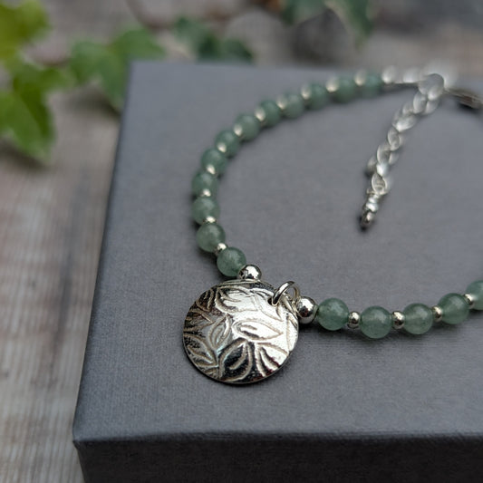 Close up of green aventurine and silver leaf disc bracelet featuring a handmade recycled sterling silver disc with a detailed leaf pattern, surrounded by soft green aventurine beads.