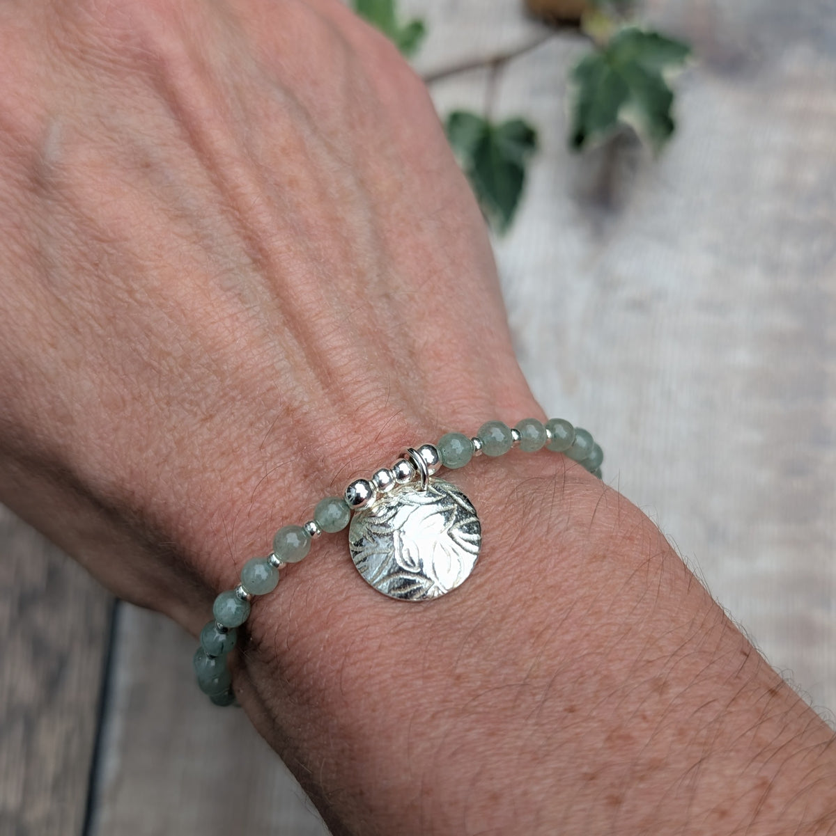 Green aventurine and silver leaf disc bracelet worn on a wrist, showing the textured sterling silver leaf charm and small green aventurine beads separated by silver spacers.