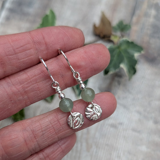 Close up of green aventurine and silver leaf earrings handmade from recycled sterling silver, featuring pale green gemstone beads and textured silver leaf discs, held between fingers.
