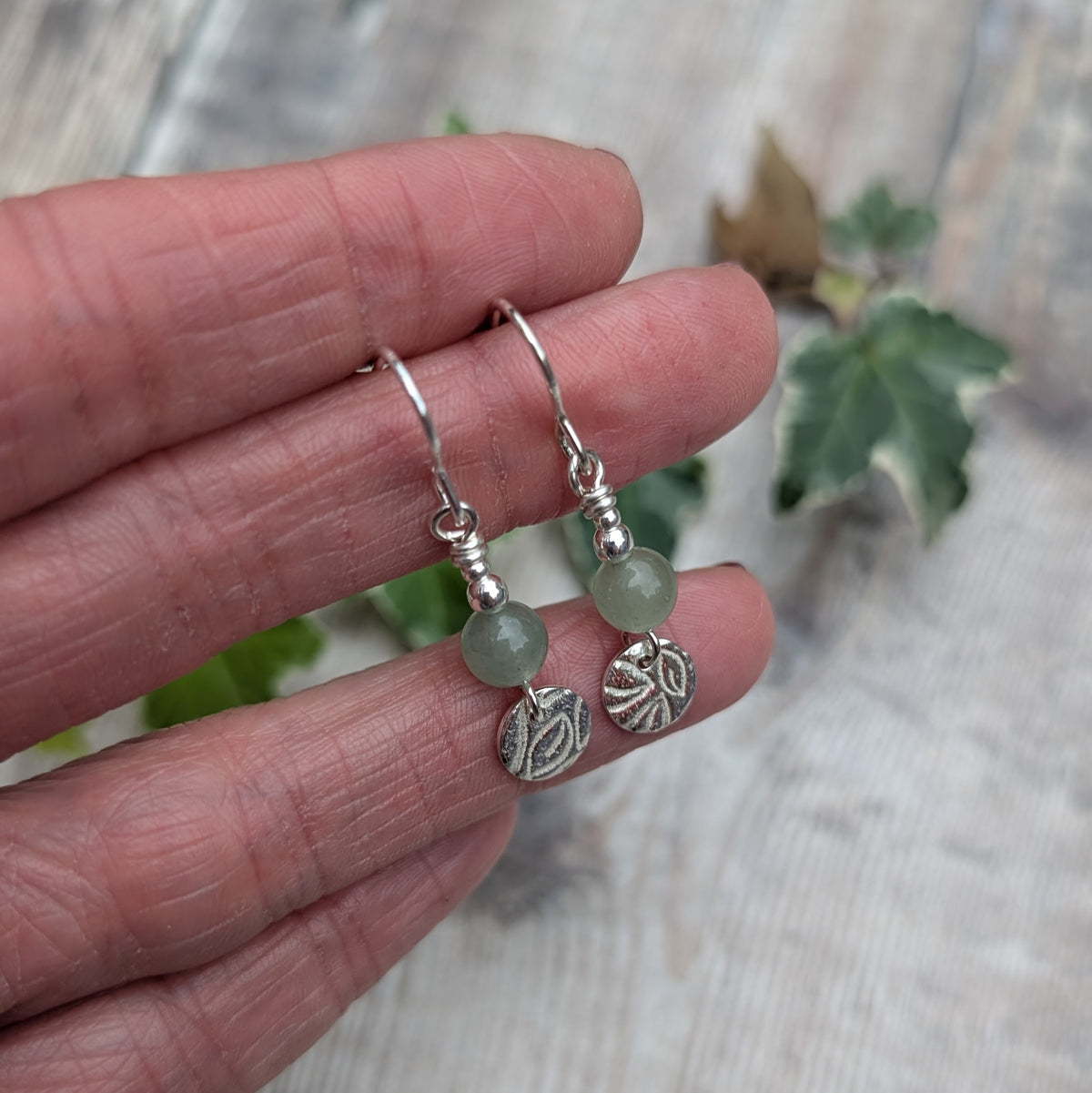 Handmade green aventurine and silver leaf earrings showing round green aventurine beads, small silver beads and leaf patterned sterling silver disc charms.