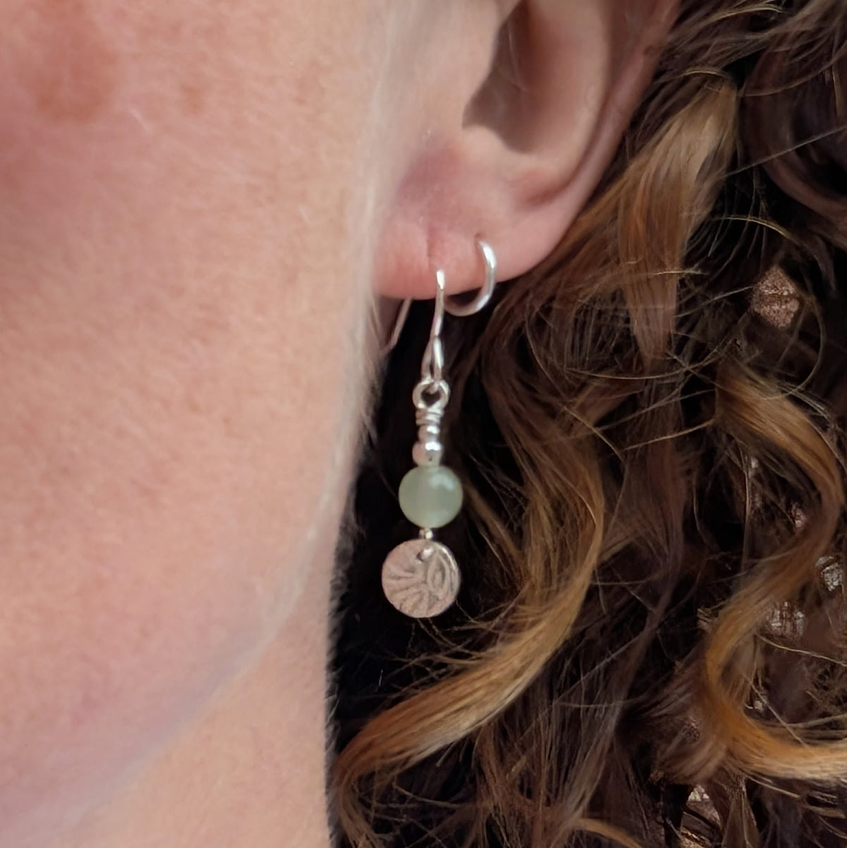 Green aventurine and silver leaf earring being worn, showing how the pale green gemstone bead and textured sterling silver leaf disc hang from the ear.