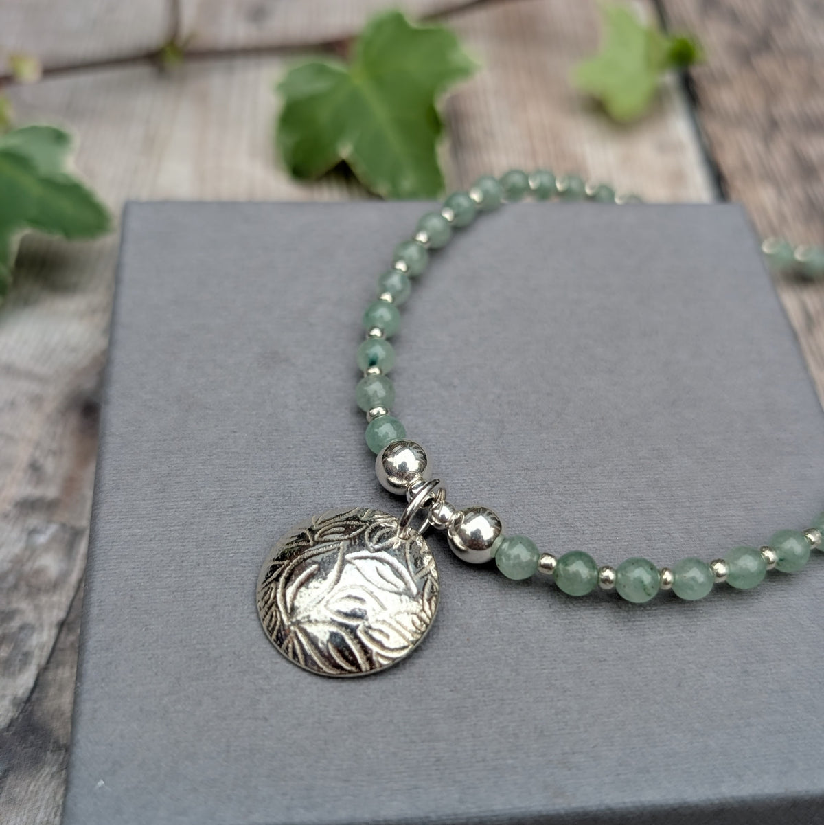 Detailed view of Green Aventurine and Silver Leaf Disc Necklace featuring a handmade recycled sterling silver disc with a raised leaf pattern, polished silver beads and soft green aventurine gemstones.