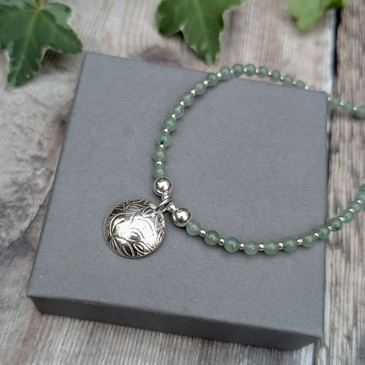 Green Aventurine and Silver Leaf Disc Necklace displayed on a grey jewellery box, showing the handmade silver leaf patterned charm and green gemstone beads separated by small silver beads.