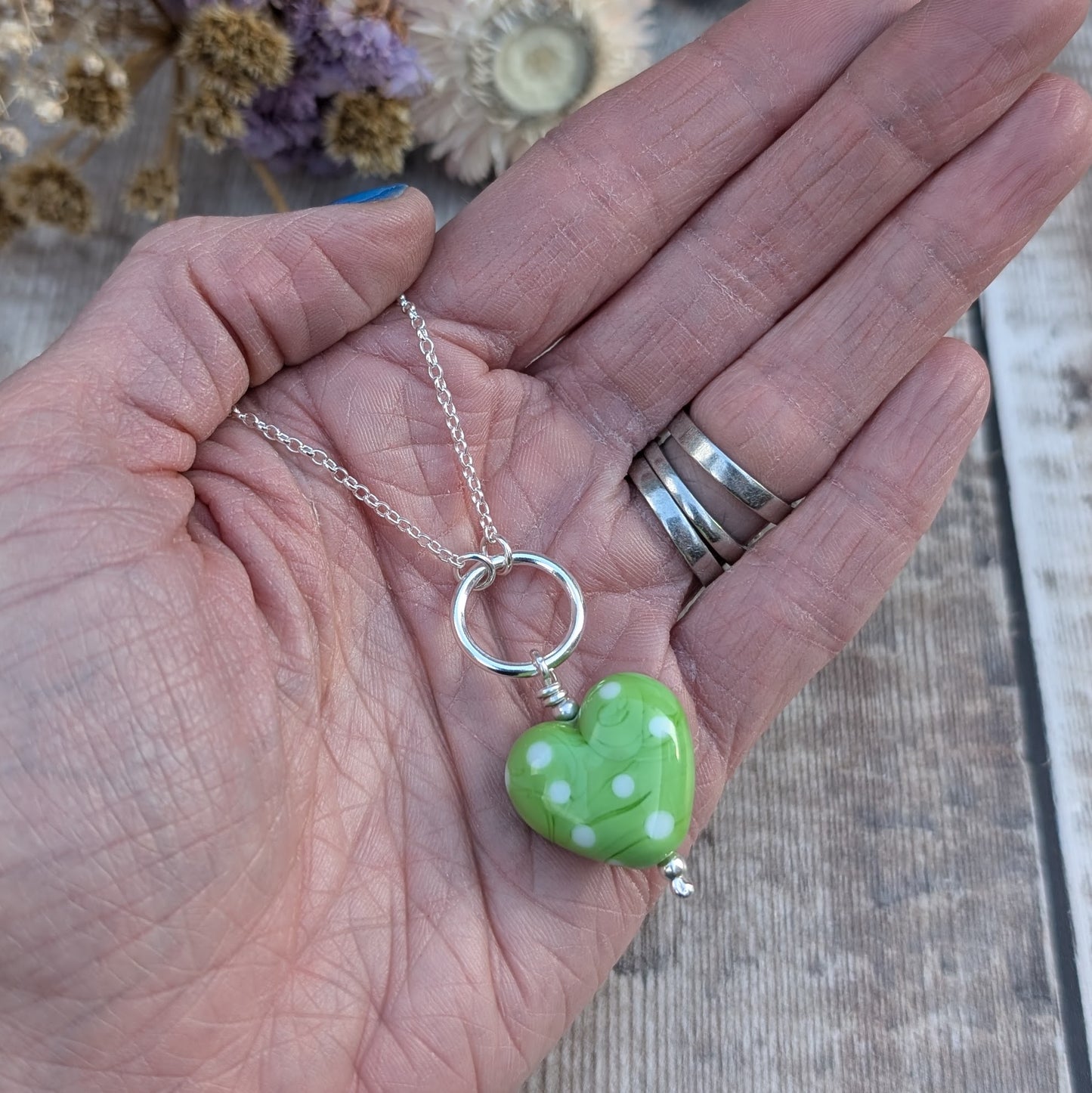 A green polka-dot Lampwork glass heart necklace with a sterling silver circle, shown in the palm of a hand to illustrate its size and detail.