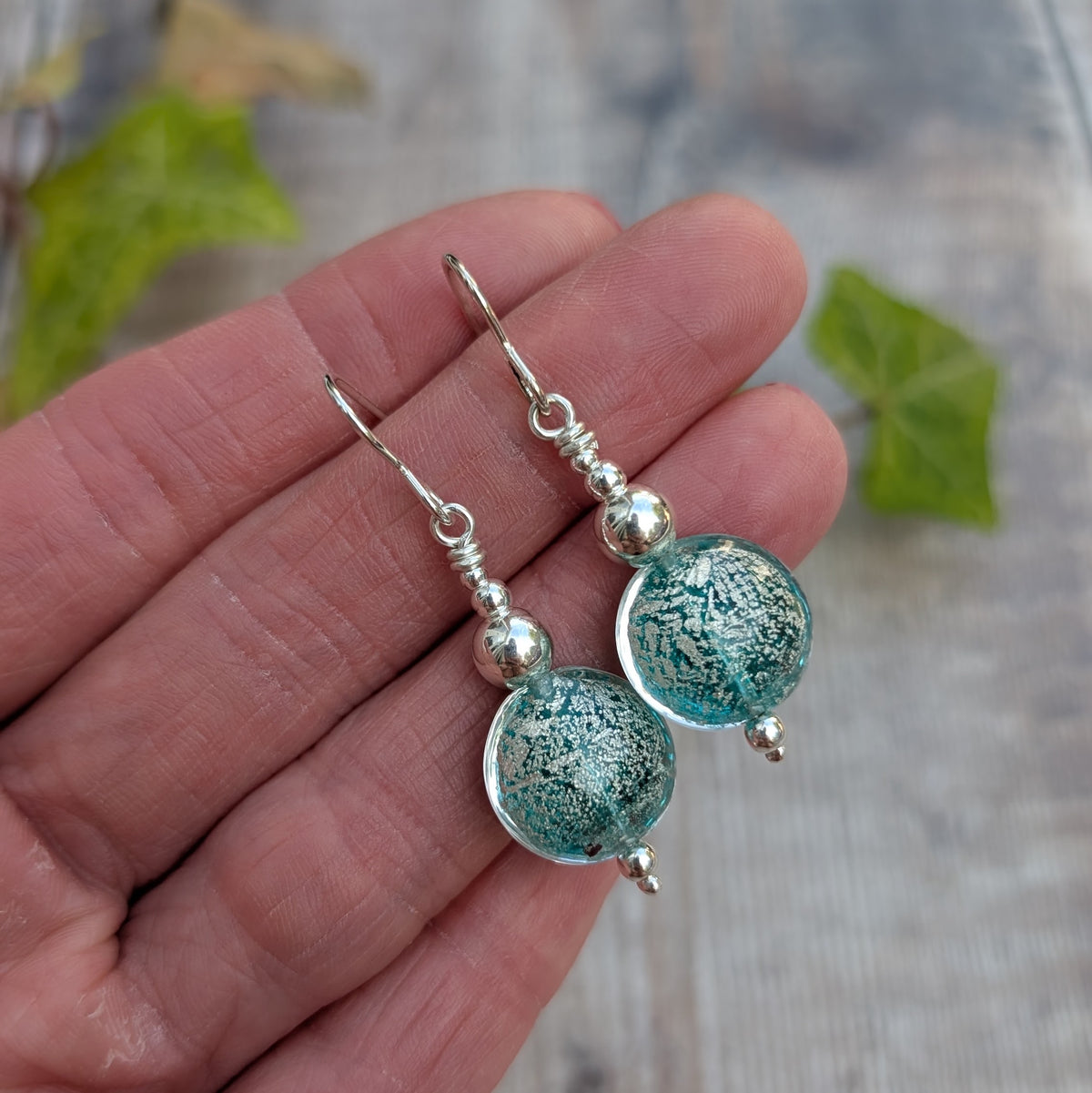 Close up of green venetian glass silver earrings held in a hand, showing the silver pattern within the handmade green glass beads.