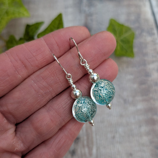 green venetian glass silver earrings handmade from recycled sterling silver with round green and silver glass beads, held in a hand.