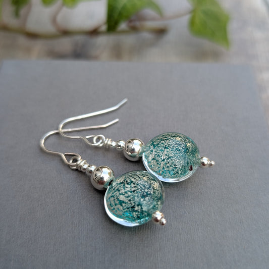 green venetian glass silver earrings lying on a grey background, showing the green and silver patterned Venetian glass beads.