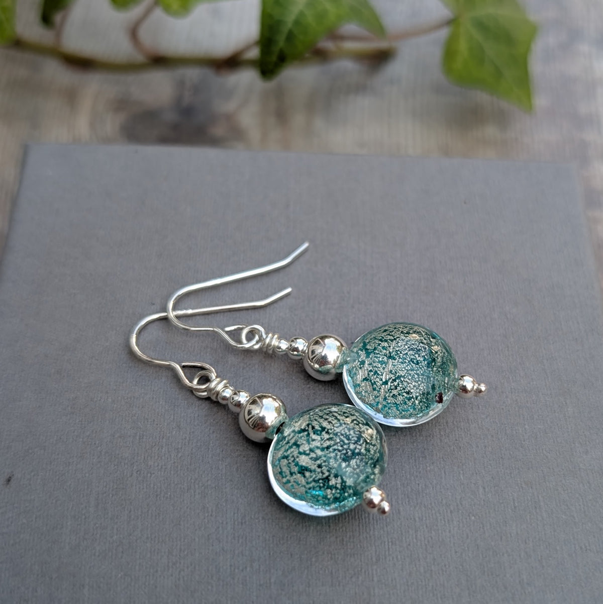 Pair of green venetian glass silver earrings displayed on a grey background with handmade glass beads and silver ear wires.