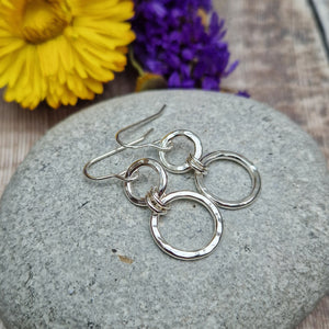 Sterling Silver two circle drop earrings. Each earring has one smaller silver open circle attached to silver earring wire. Dropping from the first open circle via two small silver hoops is a larger silver open circle. Each circle has slightly hammered texture, the largest circle measuring approximately 15mm diameter. Total drop from earlobe approximately 35mm providing lots of movement.