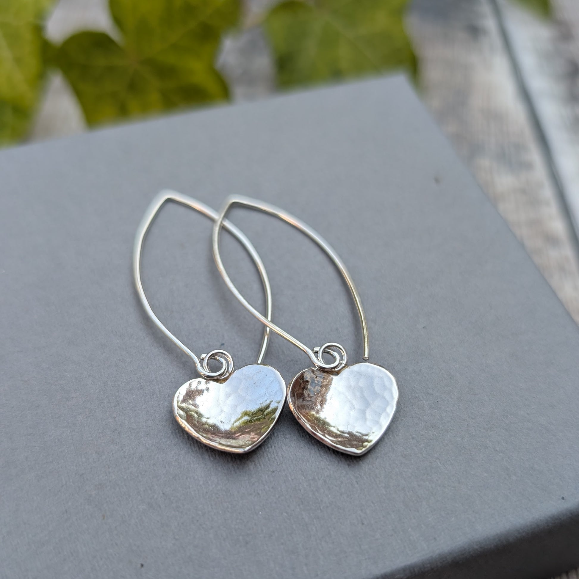 Close up of hammered silver heart long earrings handmade from recycled Sterling Silver, showing the polished heart charms and long ear wires.