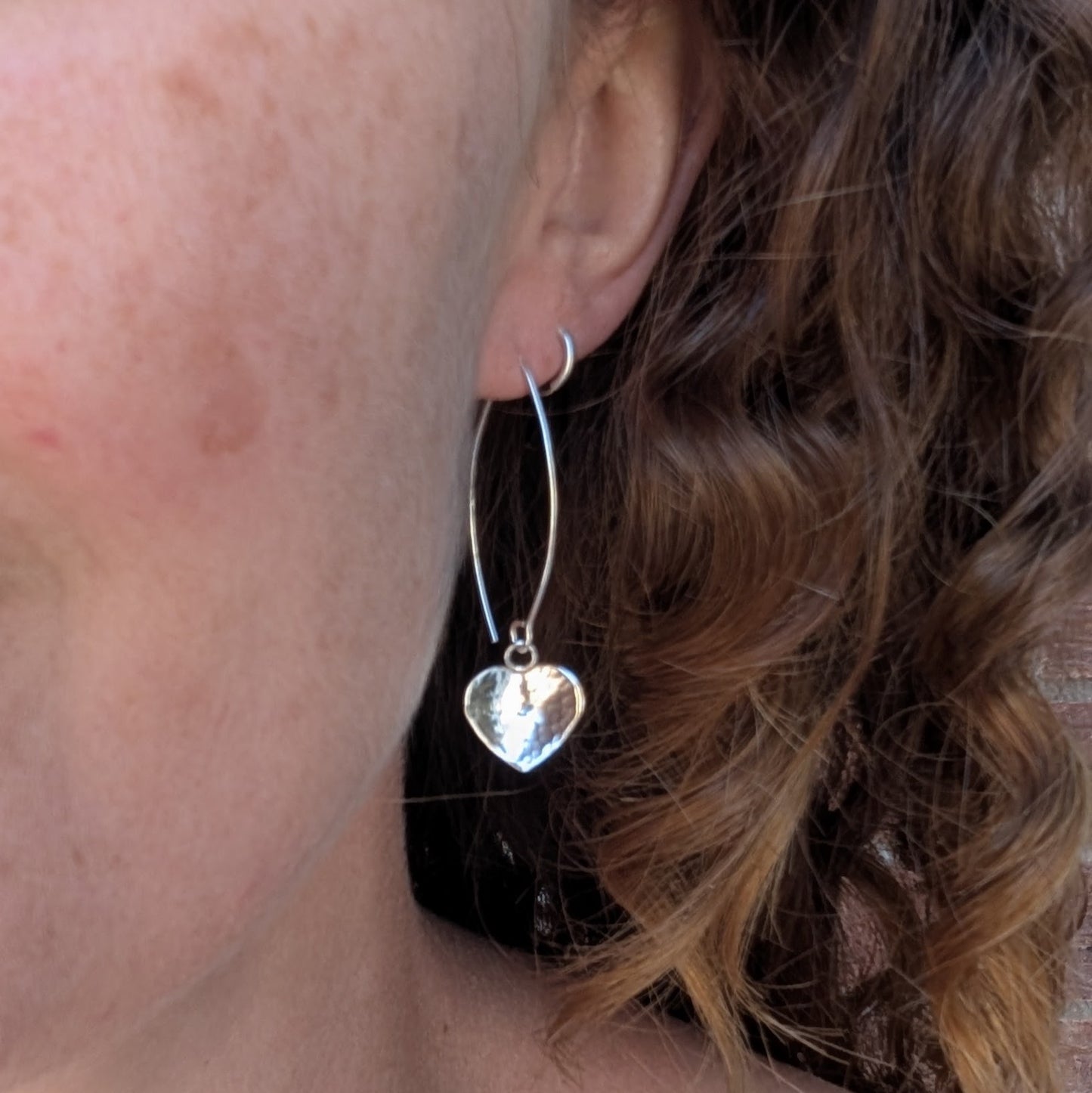 Hammered silver heart long earrings handmade from recycled Sterling Silver, worn in the ear to show their length and fit.