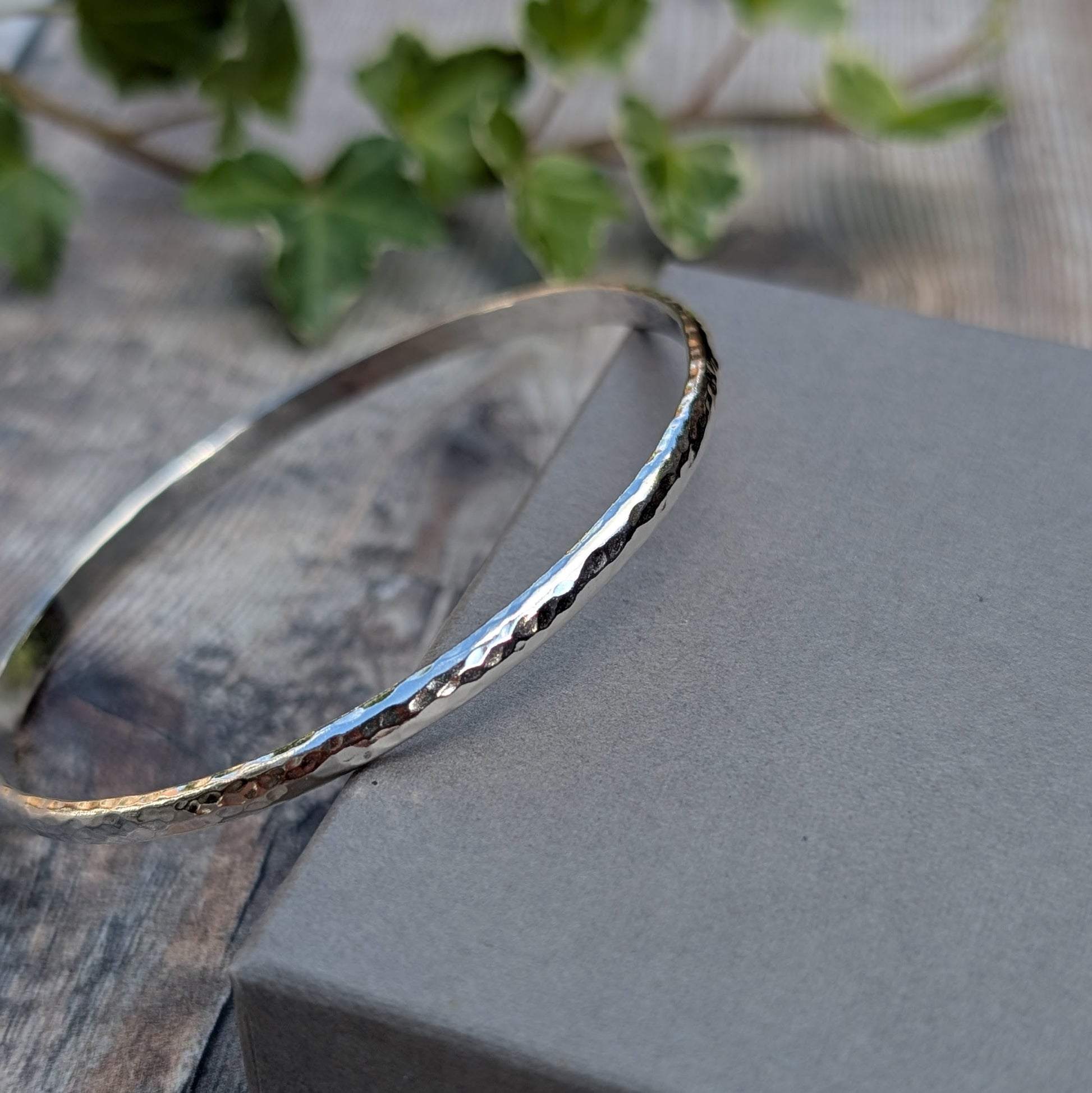 Hammered Sterling Silver D Shape Bangle handmade from recycled Sterling Silver D shaped wire leaning against a grey jewellery box, highlighting the hammered texture.