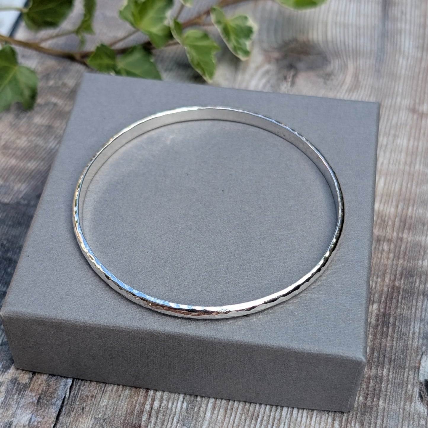 Hammered Sterling Silver D Shape Bangle handmade from recycled Sterling Silver D shaped wire, photographed from above on a grey jewellery box.