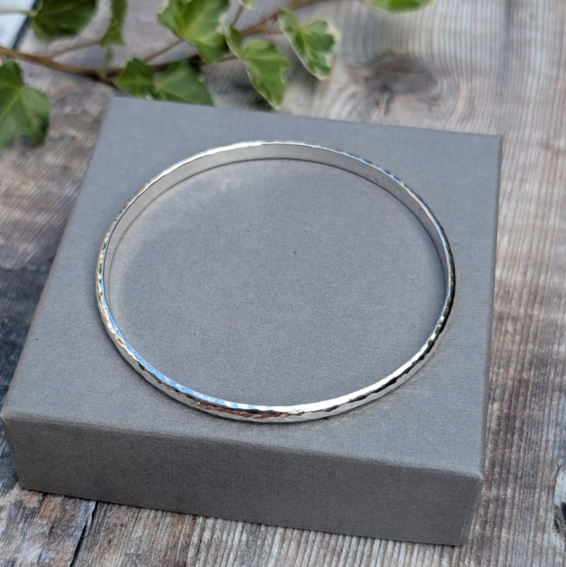 Hammered Sterling Silver D Shape Bangle handmade from recycled Sterling Silver D shaped wire, photographed from above on a grey jewellery box.