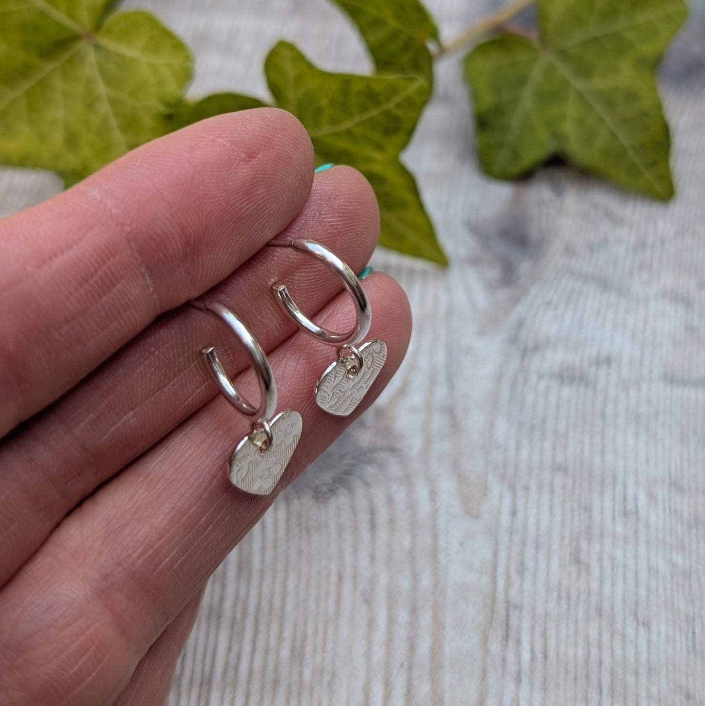 Side view of silver heart drop hoop earrings handmade from recycled Sterling Silver showing the small hoops and textured heart drops.