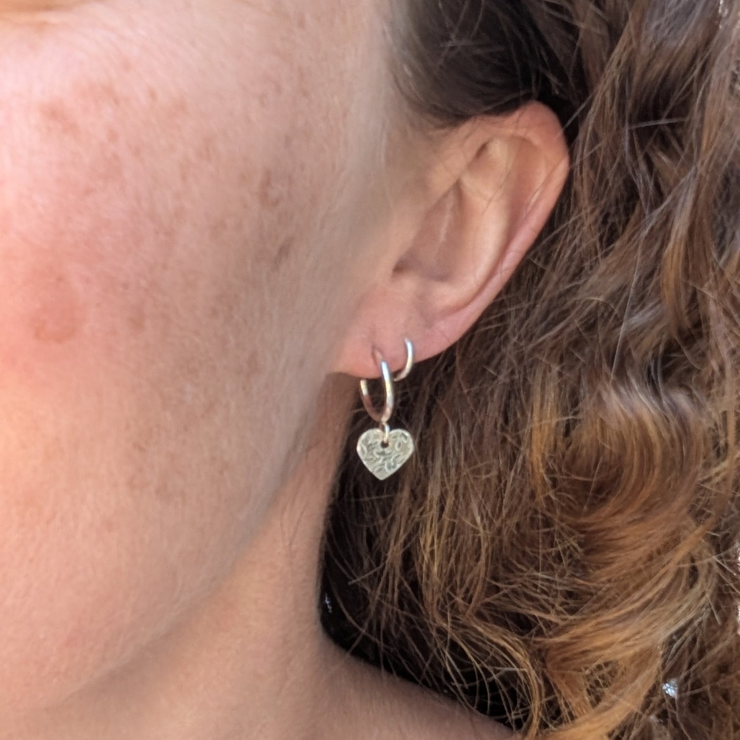 Silver heart drop hoop earrings handmade from recycled Sterling Silver worn in the ear showing their size and fit.