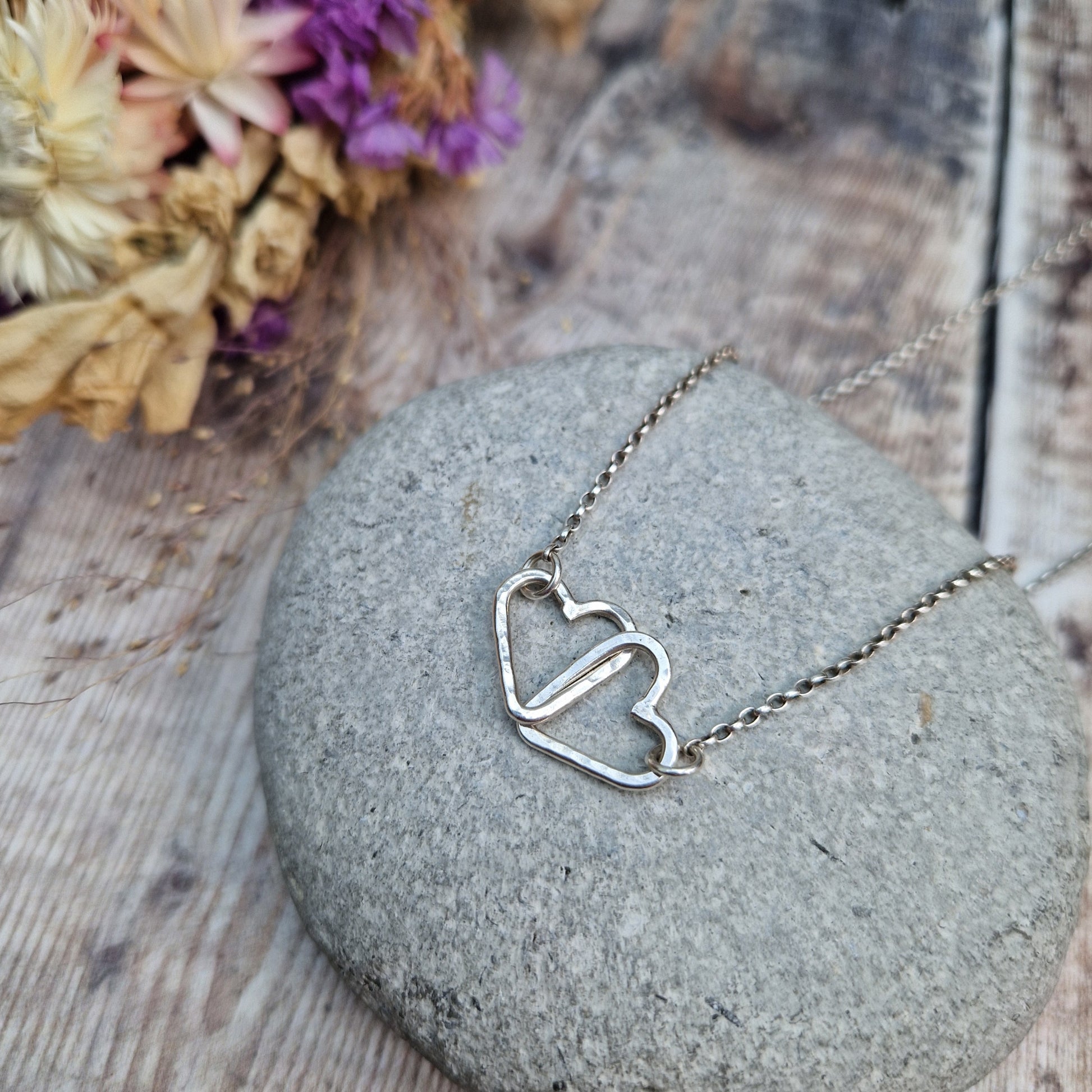 Pendant is two Sterling Silver open hearts with hammered texture, linked to each other. Suspended from silver chain via a small circle link attached to each heart.