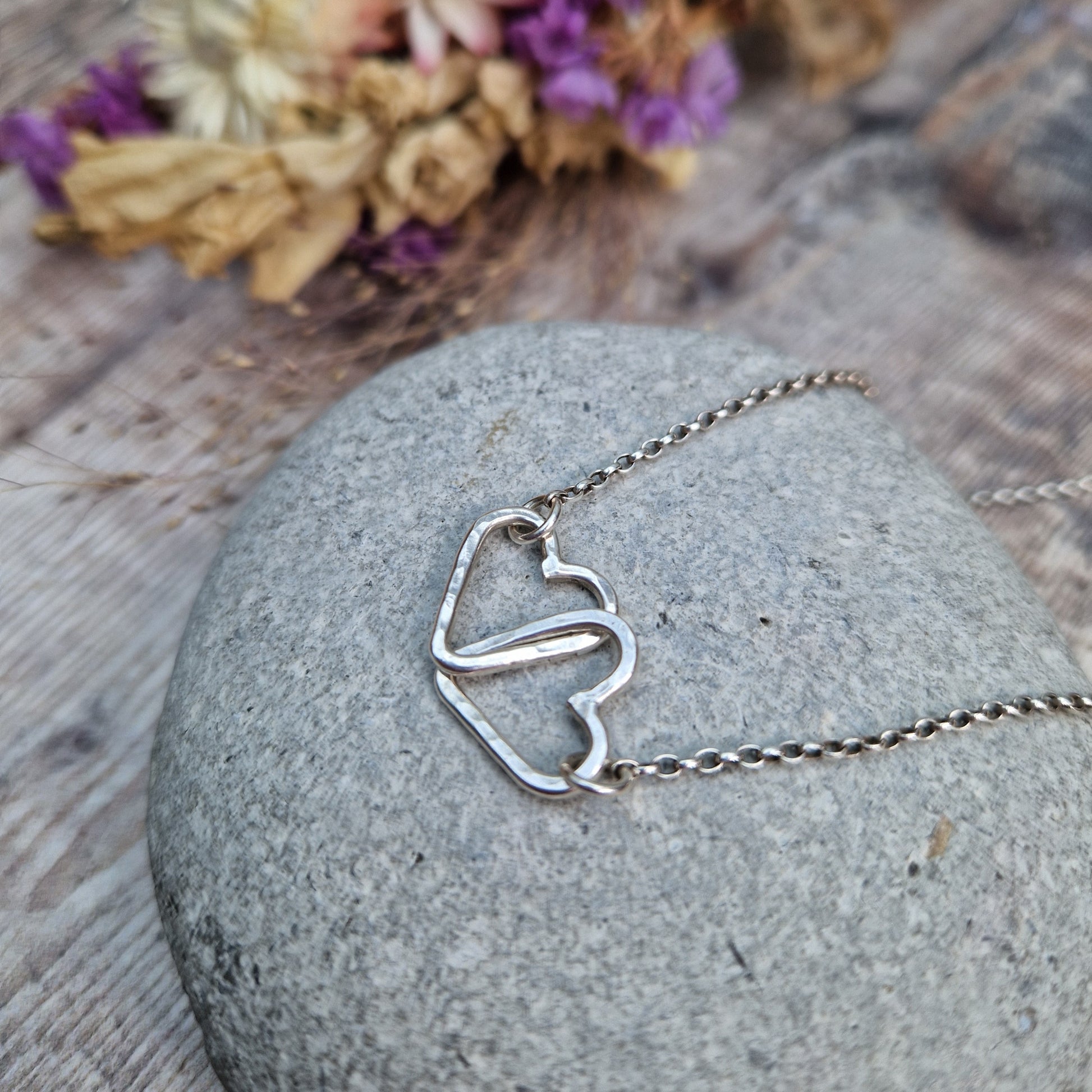 Pendant is two Sterling Silver open hearts with hammered texture, linked to each other. Suspended from silver chain via a small circle link attached to each heart.