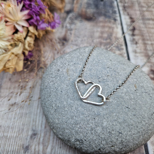 Pendant is two Sterling Silver open hearts with hammered texture, linked to each other. Suspended from silver chain via a small circle link attached to each heart.