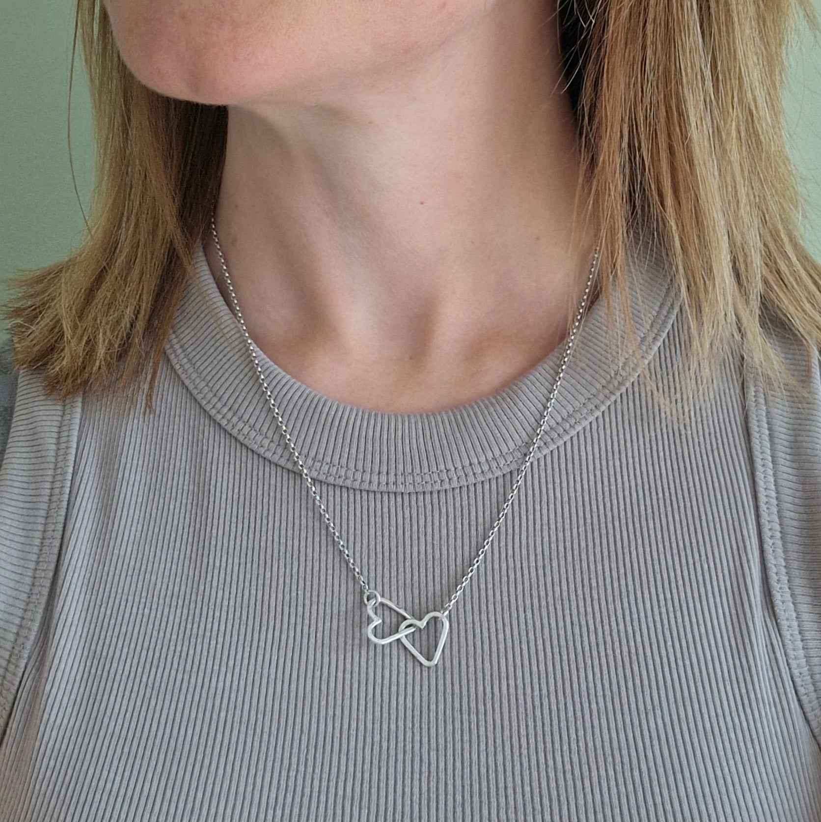 Pendant is two Sterling Silver open hearts with hammered texture, linked to each other. Suspended from silver chain via a small circle link attached to each heart.