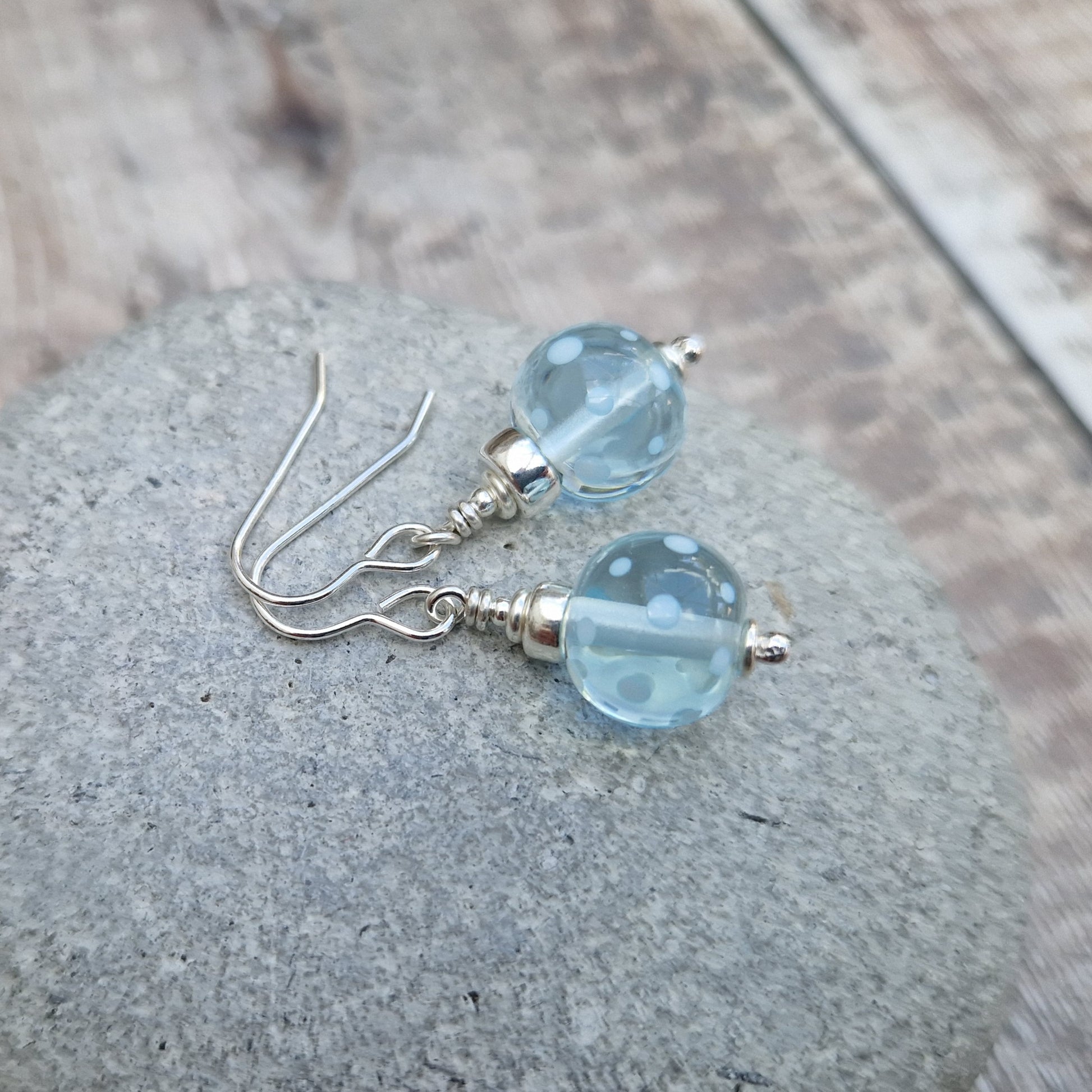 Each earring has a translucent pale blue lampwork bead suspended from silver earring wire via small, silver sphere. The lampwork bead has a small inlaid pale blue spot pattern.