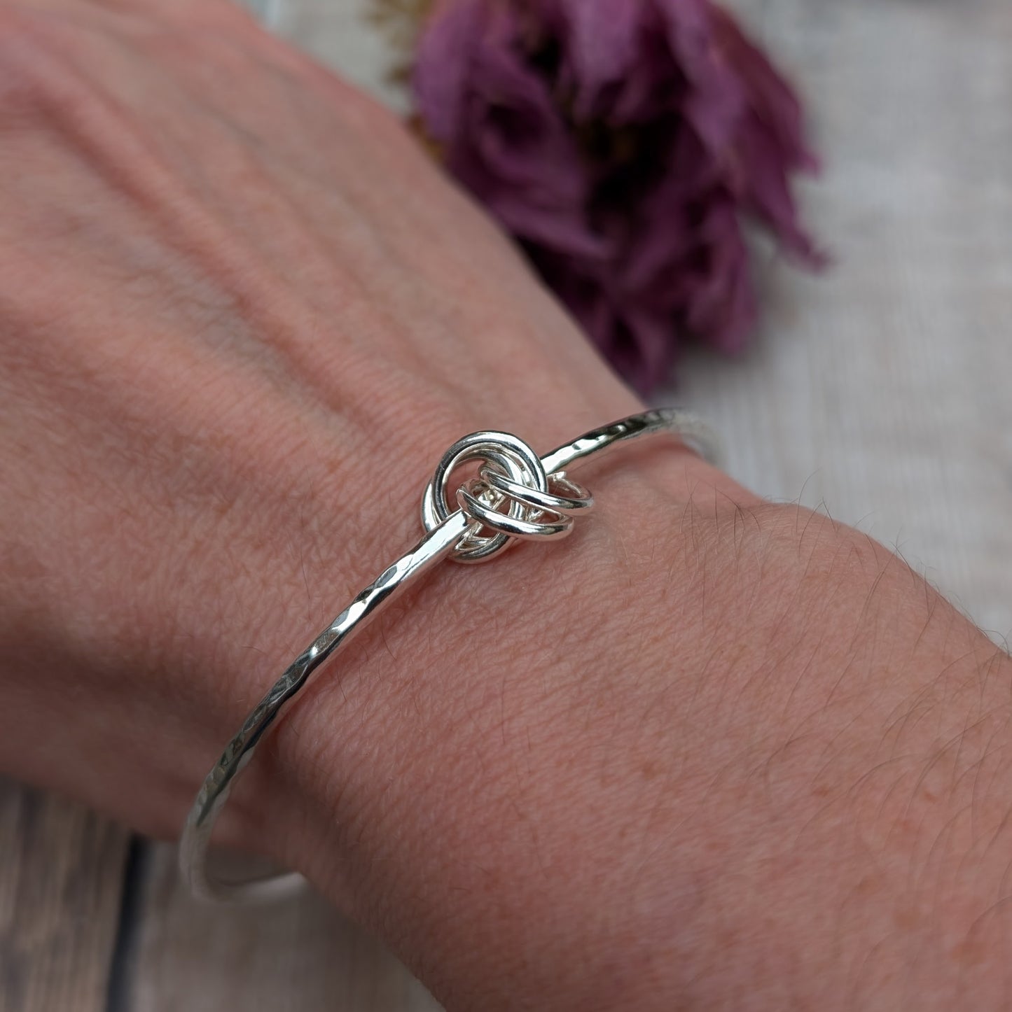 A hammered silver knot bangle worn on a wrist, showcasing its elegant knot design and subtle hammered texture.