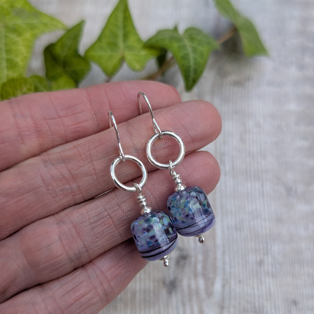 Pair of Lilac Watercolour Lampwork Glass and Silver Circle Earrings held in a hand, showing the silver circle detail and colourful glass beads.