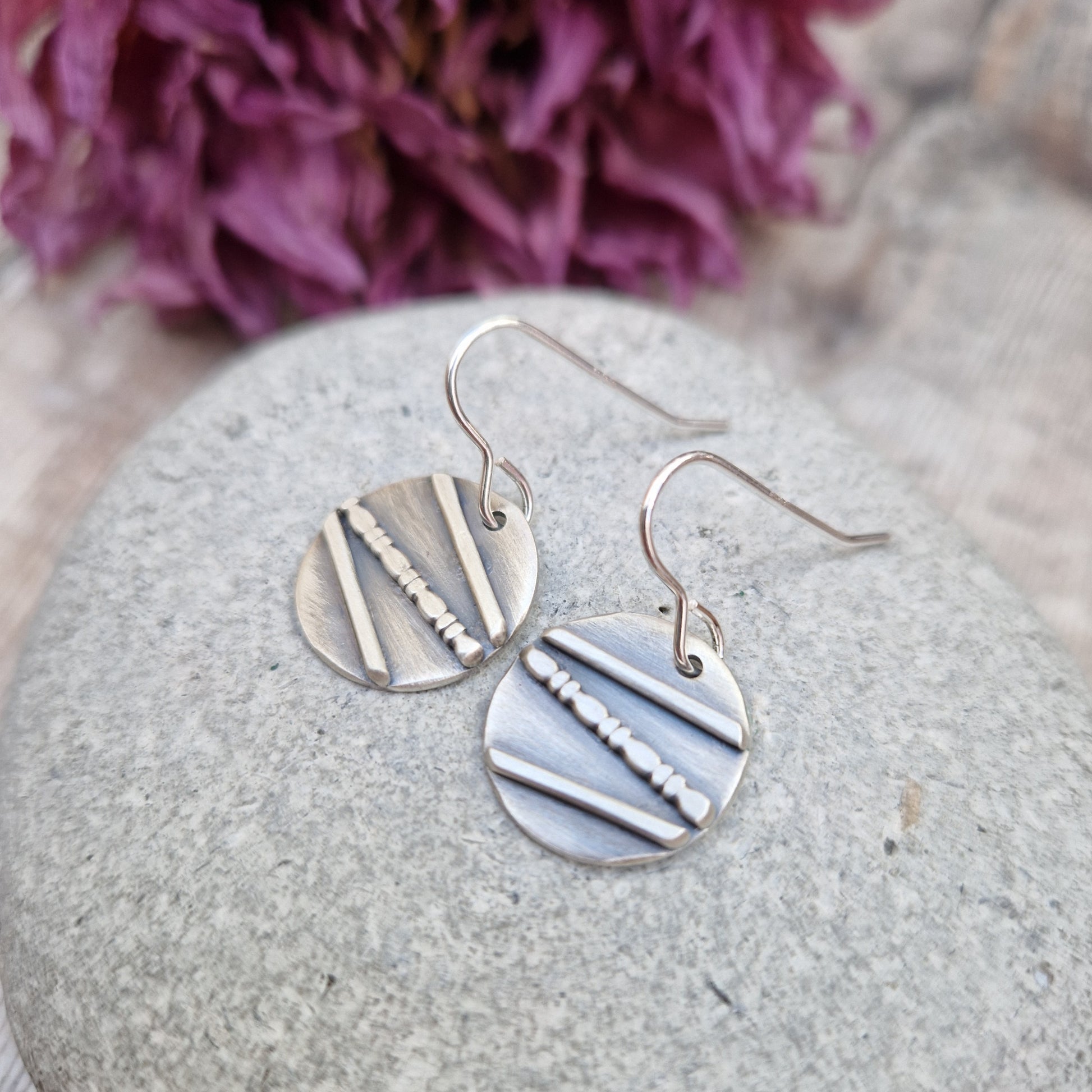 Each earring is an oxidised Sterling Silver disc with one raised straight line, one raised beaded line and one raised straight line at angles to each other across the disc, attached to earring wire.